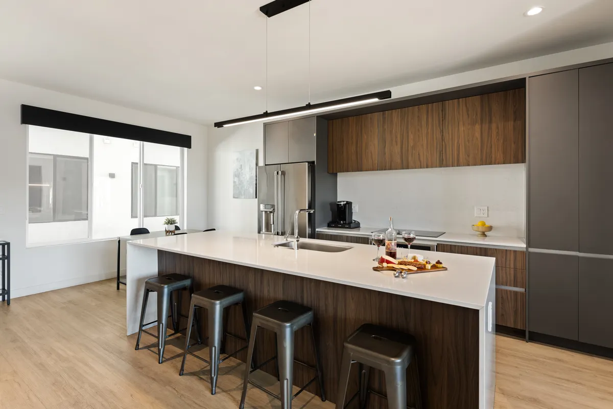 This image showcases a modern kitchen island with bar stools and contemporary appliances, highlighted by a spacious layout and inviting ambiance. The scene suggests a well-equipped, comfortable kitchen ready for everyday use, aligning with the section's promise of starter kitchen amenities.