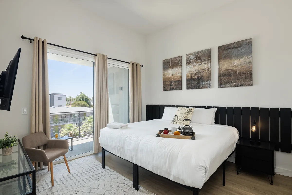 This image showcases a stylish bedroom featuring a plush king bed, elegant artwork, a cozy chair, and direct access to a private balcony. Natural light fills the space, and the inviting setup encourages both relaxation and enjoying the fresh air outdoors.