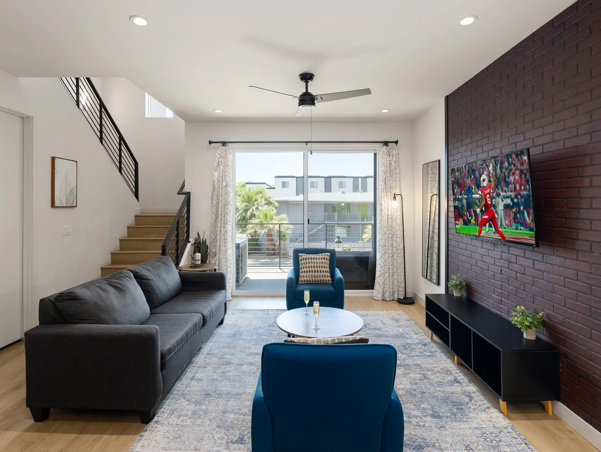 A comfortable living room scene with a plush sofa, TV, coffee table, and staircase, blending contemporary style with a relaxed ambiance. The layout suggests a welcoming space for relaxing or socializing, with the potential for pull-out sleeping arrangements.