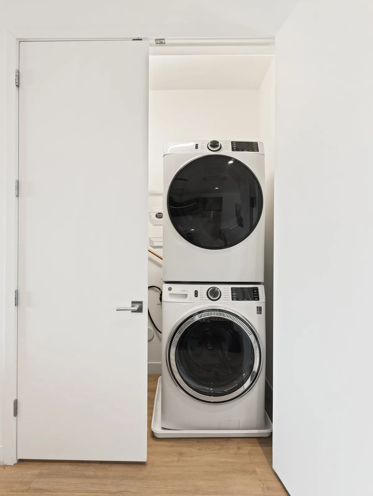 A stacked washer and dryer unit is built seamlessly into white cabinetry, surrounded by light wood flooring. The scene exudes efficiency and organization, highlighting the convenience of in-unit laundry for extended stays or day-to-day needs.