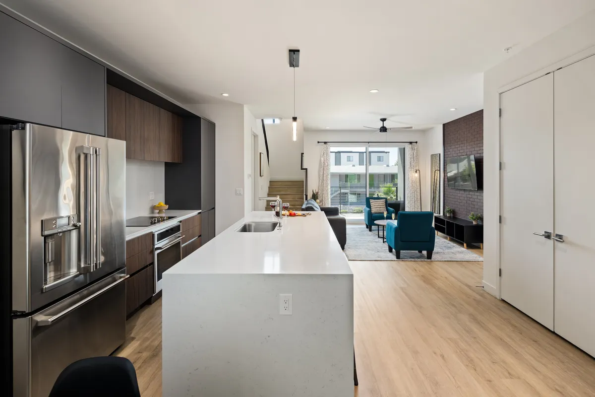 A spacious open-concept area featuring a modern kitchen with a large island, a cozy living space, and expansive windows that fill the room with natural light. The kitchen includes sleek contemporary finishes and high-end appliances, while the living area offers inviting seating and a seamless flow to the rest of the space.