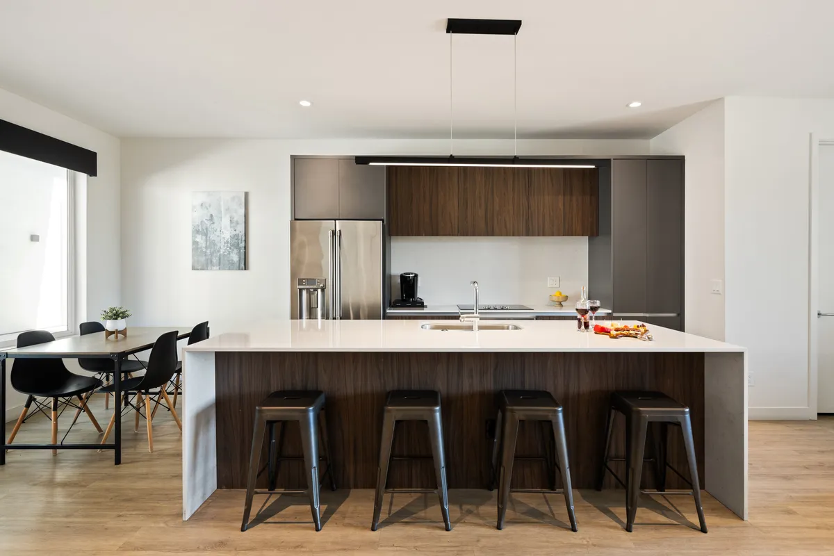 A modern kitchen with a prominent island, bar stools, stainless steel appliances, and an adjacent dining table set for a meal. The scene captures a space designed for cooking, socializing, and enjoying meals with friends or family.